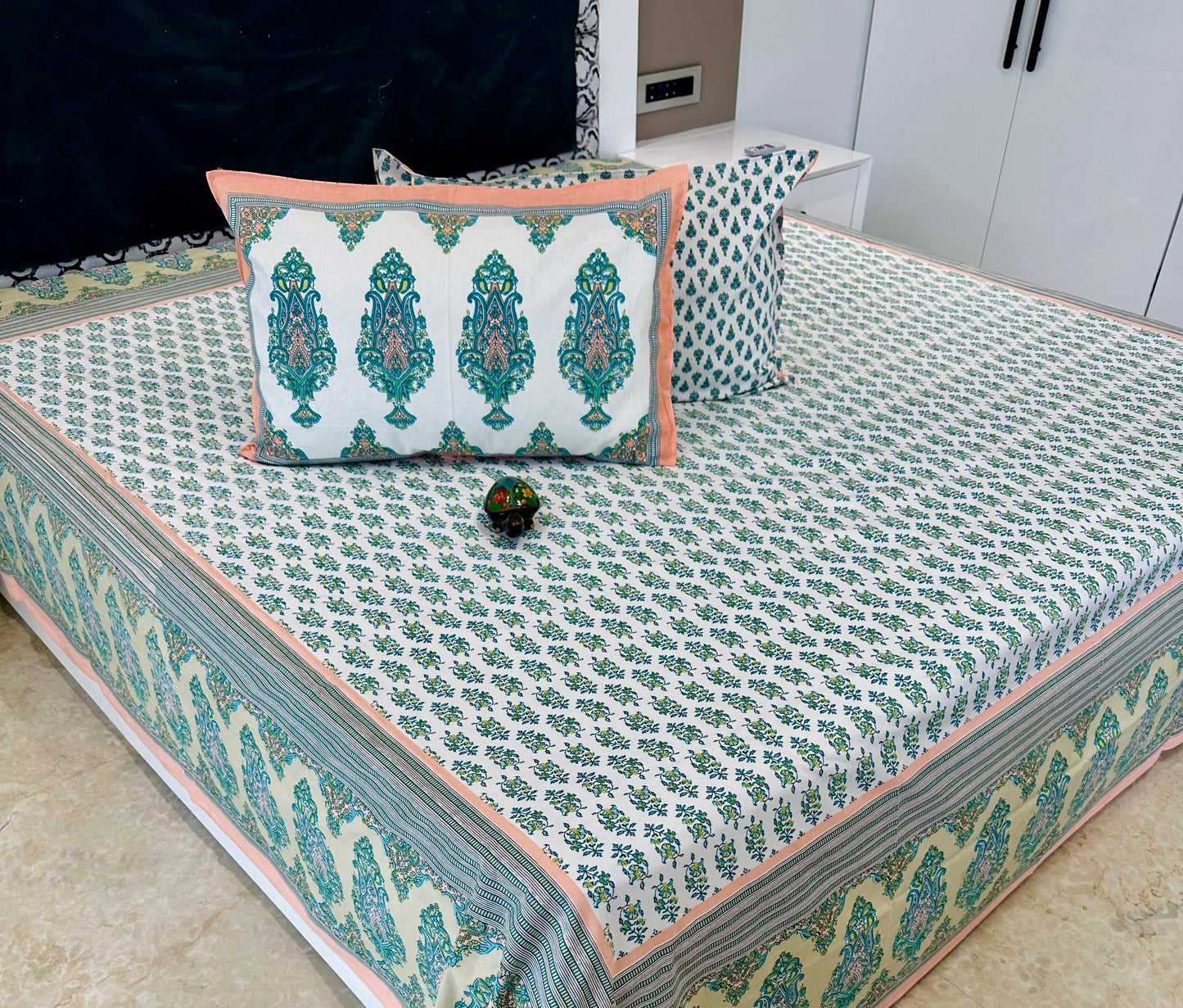 Decorative bedspread with green and pink patterns on a bed.