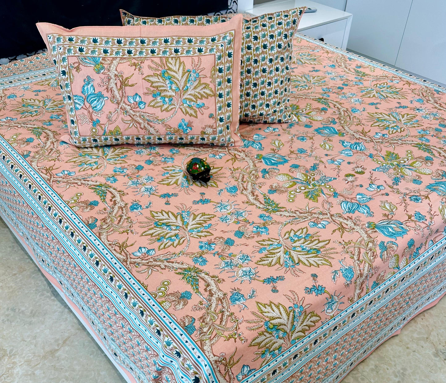 Floral patterned bedspread with matching pillows on a bed, labeled 'Shahi Collection'.